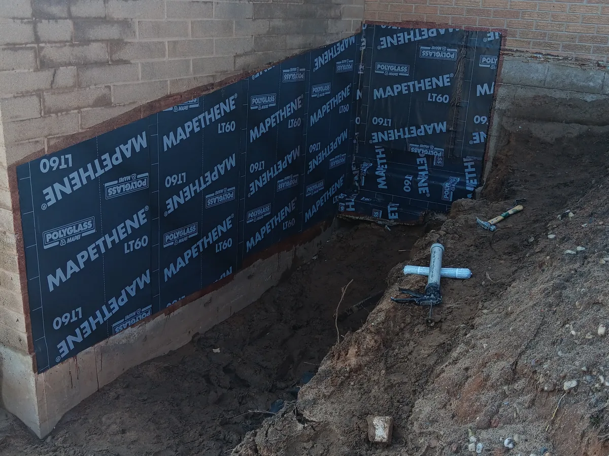 Waterproofing membrane applied across a concrete block foundation wall in a trench