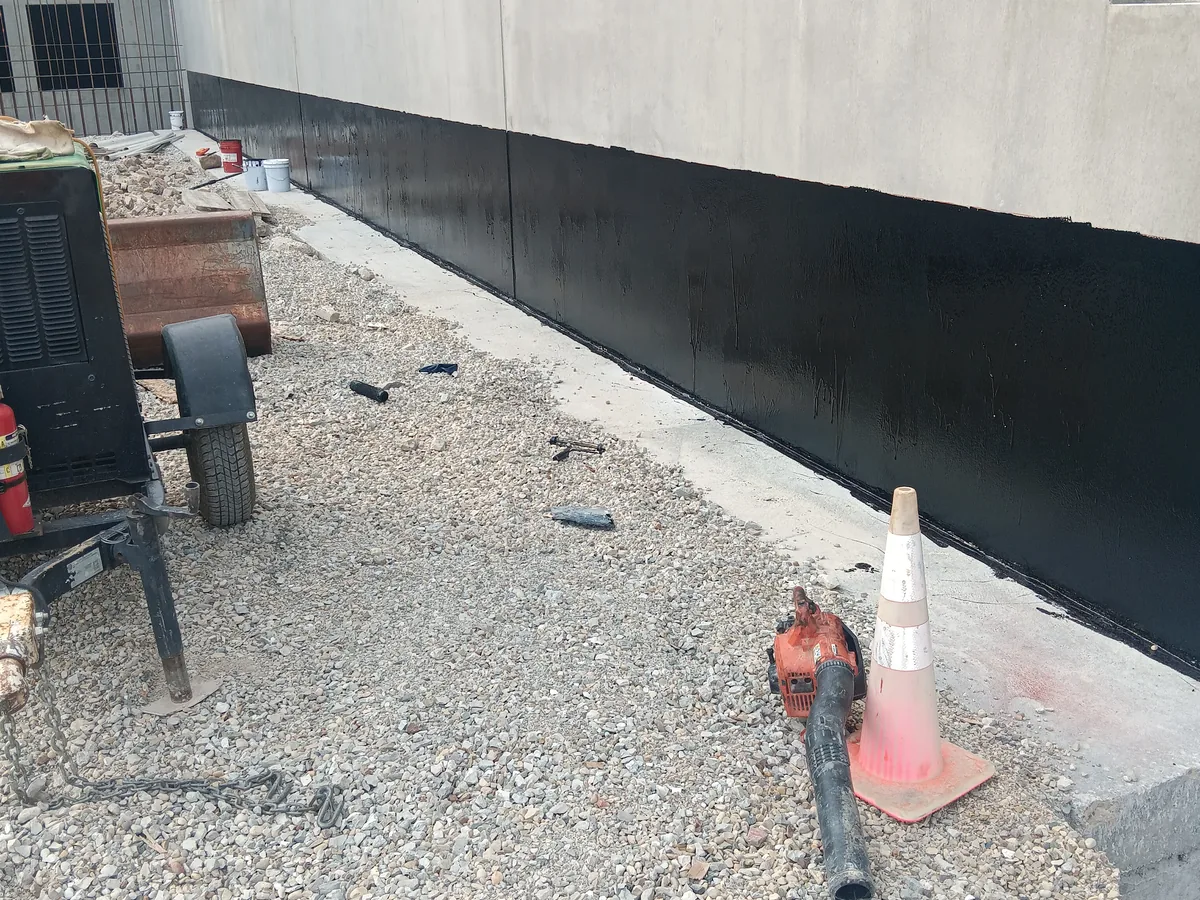Exterior foundation wall coated with black waterproofing before backfill