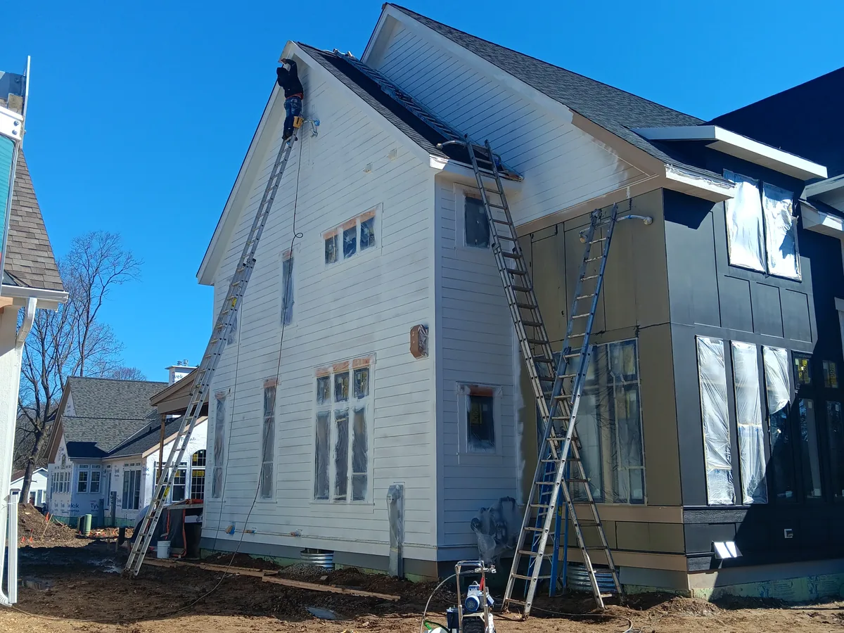 Painters on ladders working on the exterior of a two story home under construction