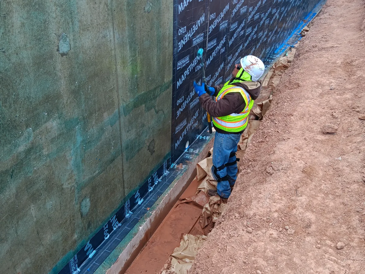 Worker applying a peel and stick waterproofing membrane to an exterior foundation wall