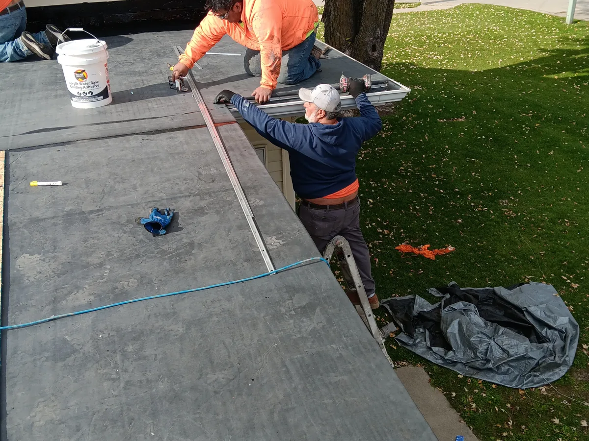 Two workers measuring and setting edge trim on a low slope roof